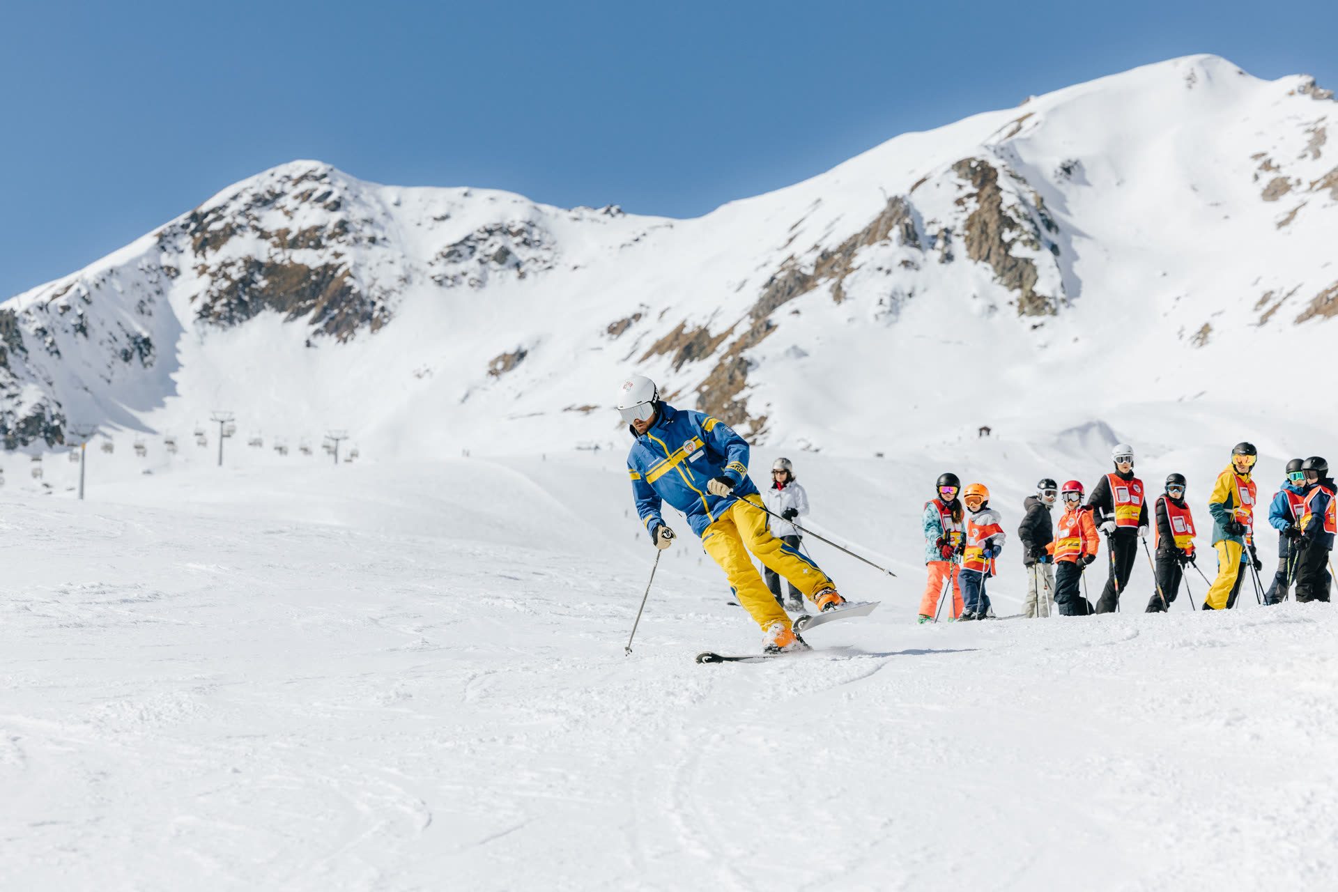 Schneesportlehrperson der Skischule Arosa fährt einer Kindergruppe auf einer breiten Piste voraus