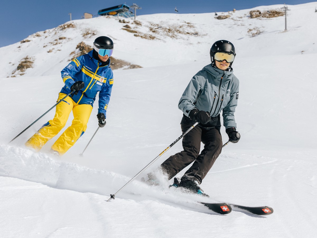 Schneesportlehrerin der Skischule Arosa fährt im Privatunterricht neben einer Jugendlichen durch einen Carving-Schwung